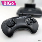 Sega Genesis controller with attached wire and a blurred game console in the background, on a white surface, with a BIG6 logo in the corner