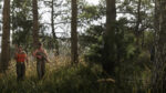 Two hunters in camo carry rifles through a sunlit pine forest with tall grass.