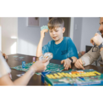 51JuLb2xi4L_AC_SL1024___163161785270583 - Video Game Depot Children play a tabletop board game at a wooden table, with cards and game pieces visible on the board.