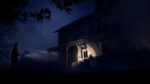 Person standing outside a dilapidated two-story house at night, shining a flashlight toward the porch.