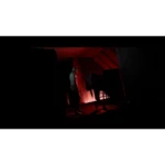 Man standing in a dark, red-lit room beside a wheeled medical cart.