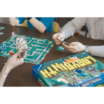 61J0WeExGhL_AC_SL1024___135471785270584 - Video Game Depot Two players at a table playing a board game; one holds cash fanned in hand, the other has cards, with a green maze board and a colorful game box nearby.
