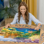 Woman smiles while assembling a colorful jigsaw puzzle at a wooden table, with scattered pieces around and a tropical landscape image completing on the board.
