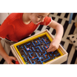 81gxGgBsNFL_AC_SL1500___188491785344548 - Video Game Depot Young girl in a red shirt plays a wooden maze puzzle with blue walls inside a yellow frame inside a cozy room.