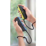 Two hands hold a blue and a yellow Nintendo Switch Joy-Con controller, connected by wrist straps, in a gaming pose.