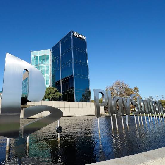 playstation headquarters - Video Game Depot Shiny PlayStation logo sculpture rising from a reflecting pool in front of a modern glass Sony office tower on a sunny day.