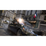 Black sedan in a city street firing from its windows during a high-speed chase; a French flag on a building in the background.