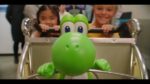 yoshi-001 - Video Game Depot Bright green cartoon dinosaur toy sits in a shopping cart, while two smiling children stand behind it.
