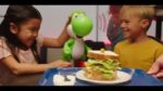 yoshi-002 - Video Game Depot Two kids smile at a table with a giant burger on a plate while a green Yoshi plush stands nearby.